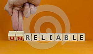 Unreliable or reliable symbol. Businessman turns wooden cubes and changes the word unreliable to reliable. Beautiful orange