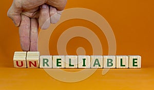 Unreliable or reliable symbol. Businessman turns wooden cubes and changes the word unreliable to reliable. Beautiful orange