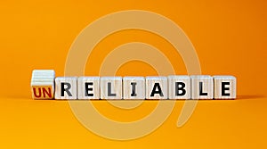 Unreliable or reliable symbol. Turned wooden cubes and changed the word unreliable to reliable. Beautiful orange background, copy