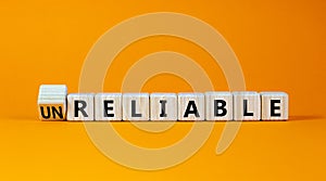 Unreliable or reliable symbol. Turned wooden cubes and changed the word unreliable to reliable. Beautiful orange background, copy