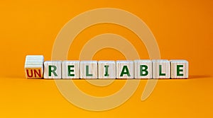 Unreliable or reliable symbol. Turned wooden cubes and changed the word unreliable to reliable. Beautiful orange background, copy