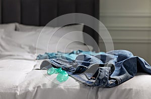 Unrolled condom and jeans on bed in bedroom. Safe sex