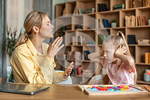 Unruly little girl closing ears with hands expressing negative emotions and looking at teacher, having private lesson