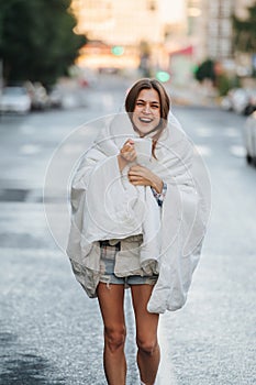 Unruly woman wrapped in blanket drinking coffee in the middle of empty city road