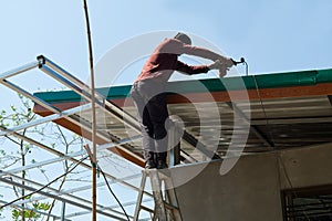 Unsafe Male Roofer Workman Using Electric Screwdriver Install Tile on Roof of New House in the Construction Site