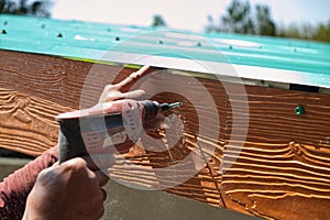 Unsafe Male Roofer Workman Using Electric Screwdriver Install Tile on Roof of New House in the Construction Site.