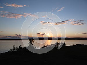 Unset on the river with blue sky and clouds and the outline of a girl on the shore