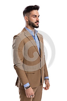 Unshaved businessman in brown suit standing in line and looking to side