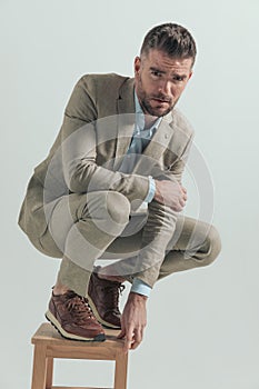 Unshaved businessman crouching on wooden chair