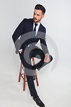 Unshaved businessman relaxing on wooden stool looks to side