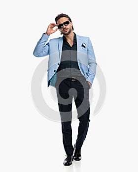 unshaved elegant man in suit with hand in pocket adjusting sunglasses