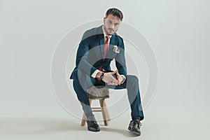 Unshaved guy in elegant suit sitting on fur chair and holding hands