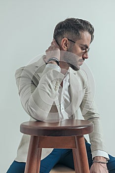 Unshaved guy with glasses holding elbow on wooden chair