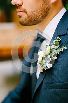 An unshaved man in a blue jacket, white shirt, tie and with a boutonniere of small roses and echeveria