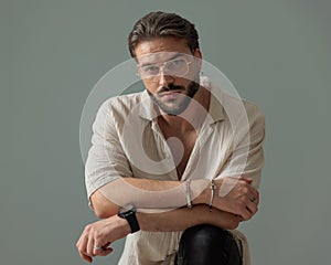 unshaved man with glasses crossing arms and holding knee up