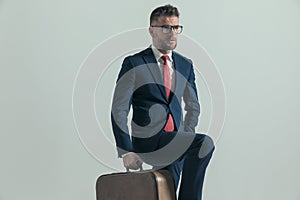 Unshaved man in his forties with luggage holding leg up and travelling