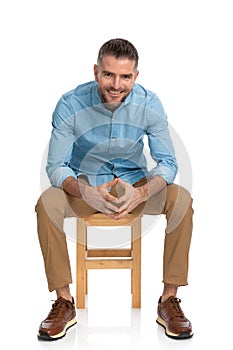 Unshaved middle aged guy holding elbows on knees and smiling