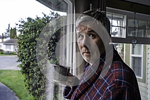 Unshaved middle aged man with messy hair holds coffee by window