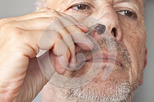 Unshaved senior man pucking nose hair with tweezers.