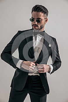 Unshaved young man looking away while buttoning black tuxedo