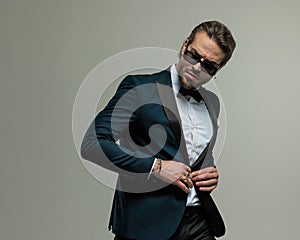 unshaved young man with sunglasses looking to side and adjusting tuxedo