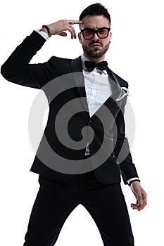 Unshaved young man in tuxedo pointing fingers to head