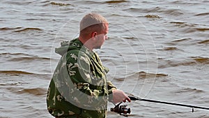 Unshaven fisherman against background of waves on river looks forward. Side view.