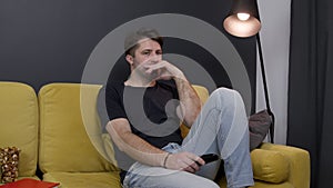 unshaven guy indifferently watching movie on TV blankly pushing remote control