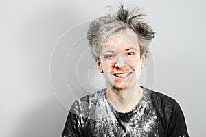 Unshaven guy with long hair smiling, sprinkled with flour and white building plaster on a gray background