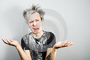 Unshaven guy with long hair soiled in plaster or flour and cry, on gray background