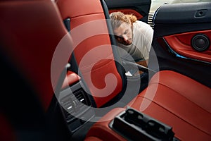 Unshaven man vacuums the inside of a car