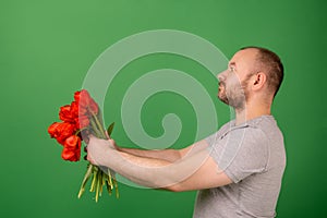 An unshaven middle-aged man holds out a bouquet of red tulip flowers to the side on a green background. Celebrate, apologize