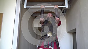 Unshaven Roman gladiator in leather armor pulls up on a horizontal bar in the corridor