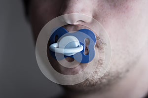 Unshaven young man holding a pacifier in his mouth