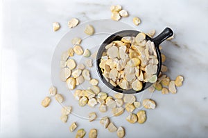 Unshelled dried small broad beans in black cup on white marble.