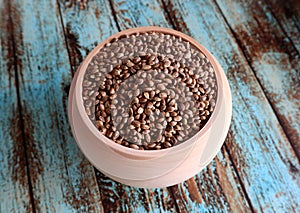 Unshelled food hemp seeds in a wooden pot on an old painted, shabby wooden background.