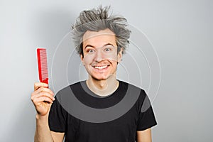 Unshorn and unshaven young guy hold comb on gray background