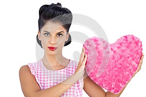 Unsmiling black hair model holding a pink heart shaped pillow