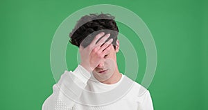 Unsmiling caucasian man showing facepalm gesture on green background