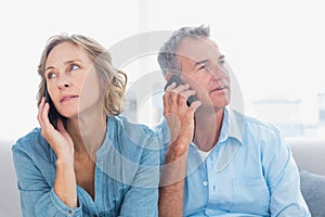 Unsmiling couple on their mobile phones on the couch