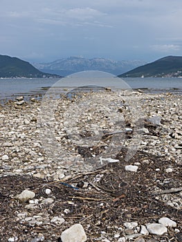 Unsorted garbage on pebble of sea shallow with medical mask, paper, grass, plastic and other junk front view sea landscape