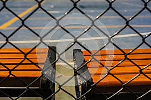 Unstoppable warm color, orange-red bench by the open-air cement basketball court inside the barbed wire