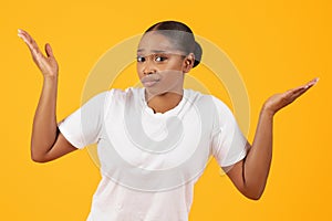 Unsure Puzzled Black Woman Shrugging Shoulders Against Yellow Studio Backdrop