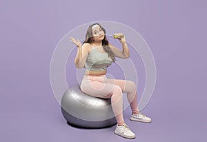 Unsure sad plus size european millennial lady in sportswear doubting whether there burger sitting on fitness ball