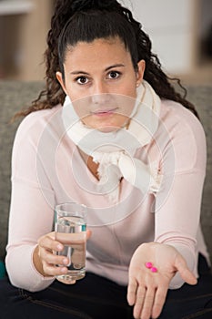 unsure woman holding two pink tablets and glass water