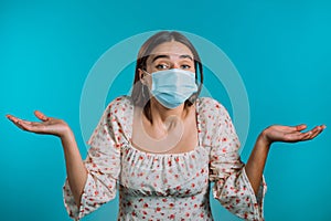 Unsure woman in medical mask shrugs her arms, makes gesture of I don`t know, care, can`t help anything . Girl on blue