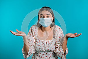 Unsure woman in medical mask shrugs her arms, makes gesture of I don`t know, care, can`t help anything . Girl on blue