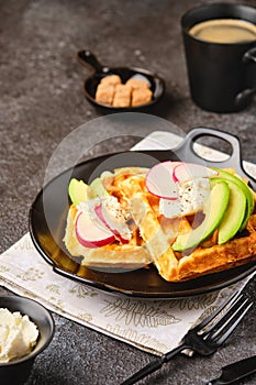 Unsweetened cheese waffles with cream cheese, avocado and radish slices on a black plate on a dark concrete background