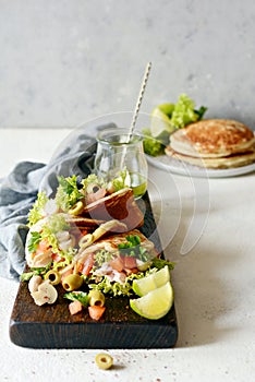 Unsweetened pancakes with turkey, lettuce, tomatoes, pickled mushrooms, olives and greens in the form of tacos on a wooden board.