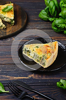 Unsweetened pastries, sliced quiche with spinach, oyster mushrooms, egg filling and cheese on a black plate on a dark wooden